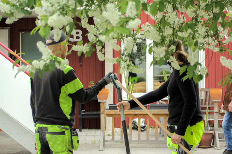 Två personer som står utomhus med trädgårdsverktyg.