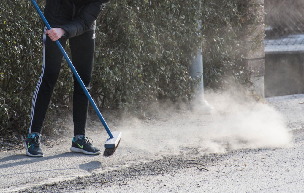 Person som sopar grus och sand på en trottoar.