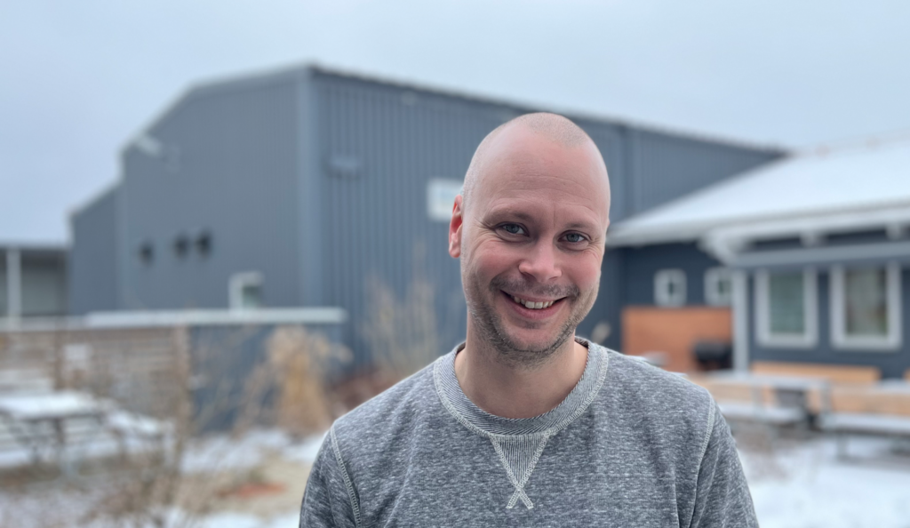 Profilbild på Daniel ståendes utomhus med en grå byggnad i bakgrunden.